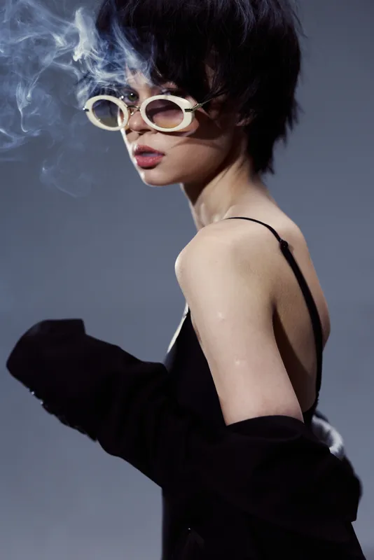 Stylish woman wearing sunglasses with smoke background, dark outfit, and short hair in moody lighting