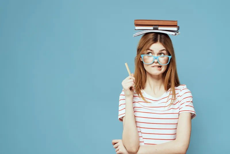 Студентка держит книги на голове на фоне синего цвета, что символизирует научное образование