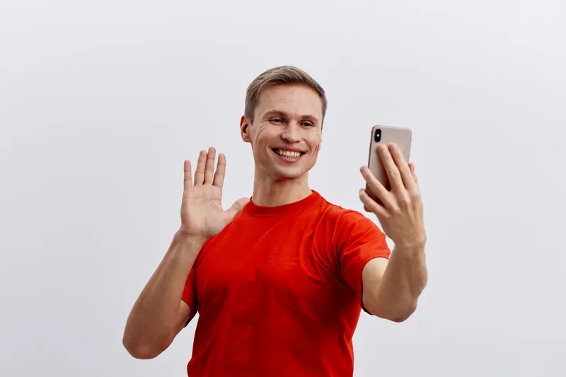 smiling man waving hand hold smartphone use video call in red t-shirt isolated on white background communication technology concept