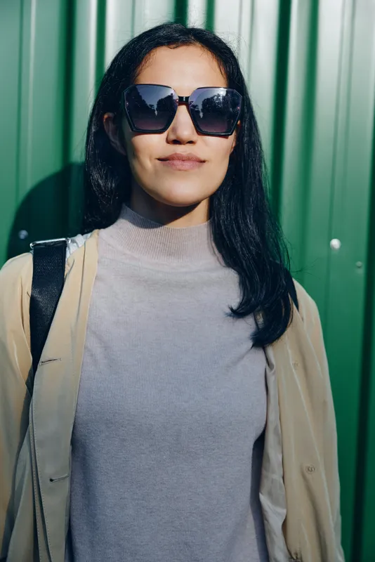 Sunglasses worn by a stylish woman against a green panel backdrop, casual chic outfit and confident pose, urban fashion vibe with bold eyewear and minimalist look in bright light