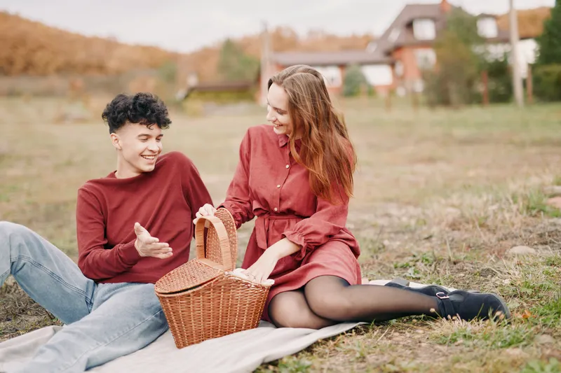 Young couple sharing a relaxed outdoor picnic, laughing and interacting naturally on a blanket, capturing emotional closeness and authenticity in a candid everyday moment.
