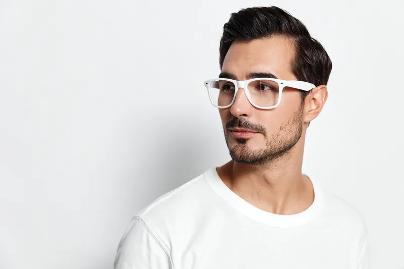 Stylish man wearing white glasses and a plain t-shirt poses confidently against a neutral background. Modern lifestyle concept for fashion and self-expression.