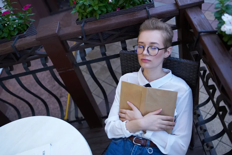 Студент с книгой в руках на открытом воздухе в летнем кафе, отдых и общение