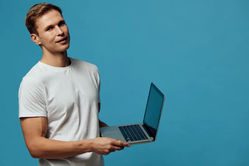 Young man working with laptop using artificial intelligence technology in casual white t-shirt on blue background digital nomad concept