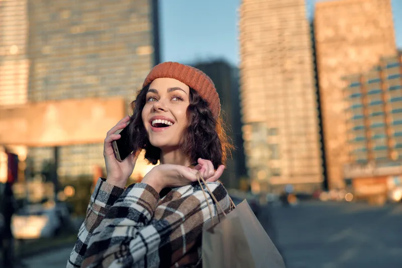 Woman shopping with phone and smile in city portrait, urban lifestyle moment during golden hour glow, candid authenticity and mindful living captured with emotional storytelling vibe.