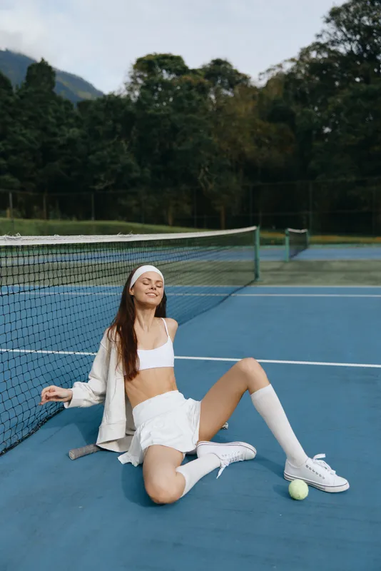 Stylish young woman in sportswear on a tennis court, enjoying a moment of relaxation and joy, showcasing confidence and athleticism