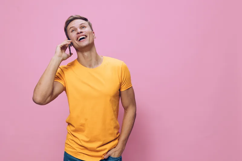 Smiling young man talking phone orange t-shirt pink background cheerful positive emotion communication digital nomad concept