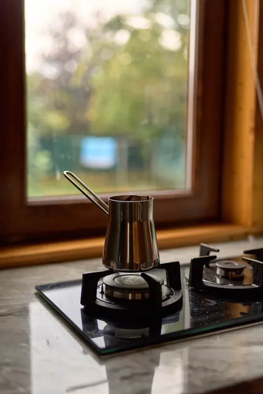 coffee cezve stovetop kitchen window morning marble gas, metal cezve boiling on stovetop near wooden window, warm morning light, cozy home brewing scene