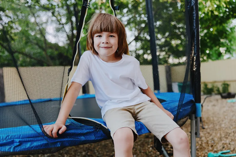 Happy boy enjoying time on a trampoline, surrounded by lush greenery and a sunny atmosphere. A perfect moment of childhood joy captured outdoors.