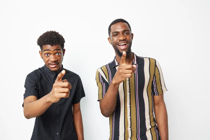 Two black men pointing playfully at the camera, showcasing their vibrant personalities through fun expressions and fashionable outfits, perfect for a cheerful vibe.