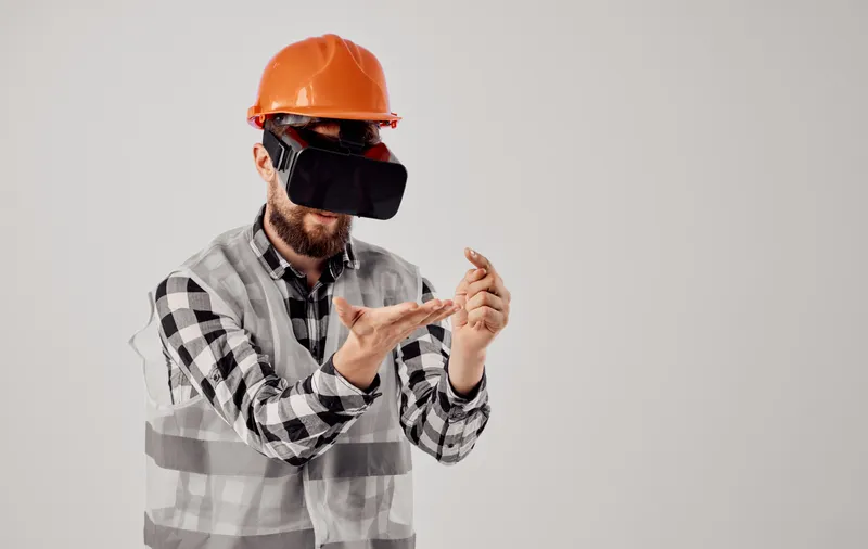 Архитектор в 3D-очках виртуальной реальности жестикулирует руками, на голове оранжевая каска