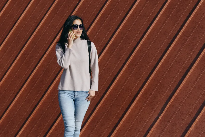 Casual woman posing against a diagonal wooden wall, wearing sweater, jeans and sunglasses, relaxed street style for fashion, outdoor lifestyle, confident pose and urban backdrop