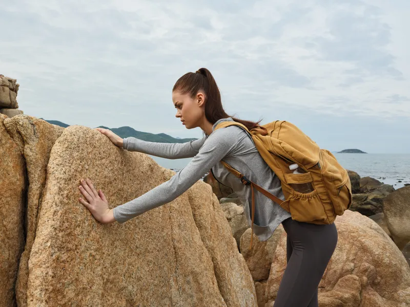 Young woman with a backpack exploring rocky beach, showcasing determination and adventure in a natural setting, suitable for outdoor activities and travel themes