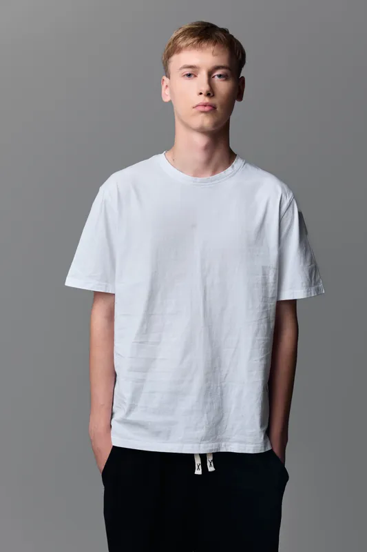 White tshirt worn by a young man in a neutral studio setting, casual minimalist fashion for everyday wear, clean lines and relaxed stance, simple wardrobe essential for lifestyle and catalog