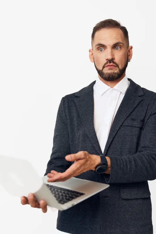 A focused professional man stands against an isolated colored background, presenting calm confidence while using a laptop to convey business insight and forward momentum.
