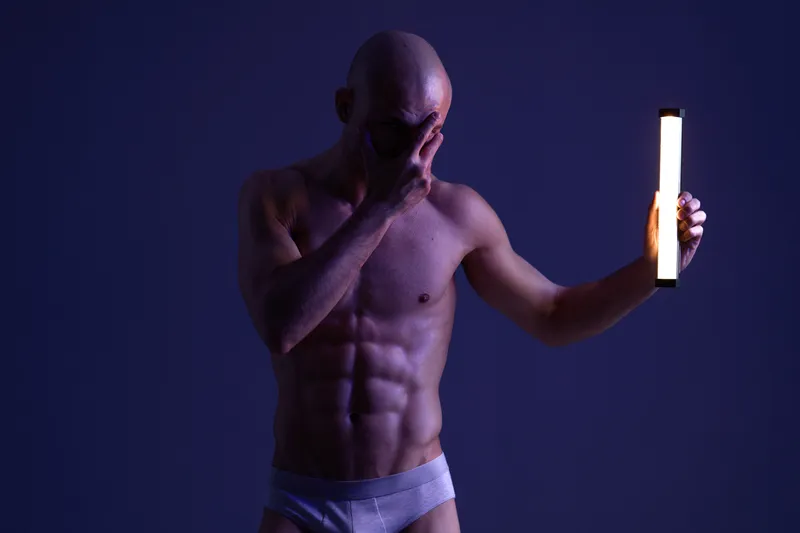 Muscular man posing with a light, showcasing strong physique and dramatic expression in a dark atmosphere. This is a striking black and white image.