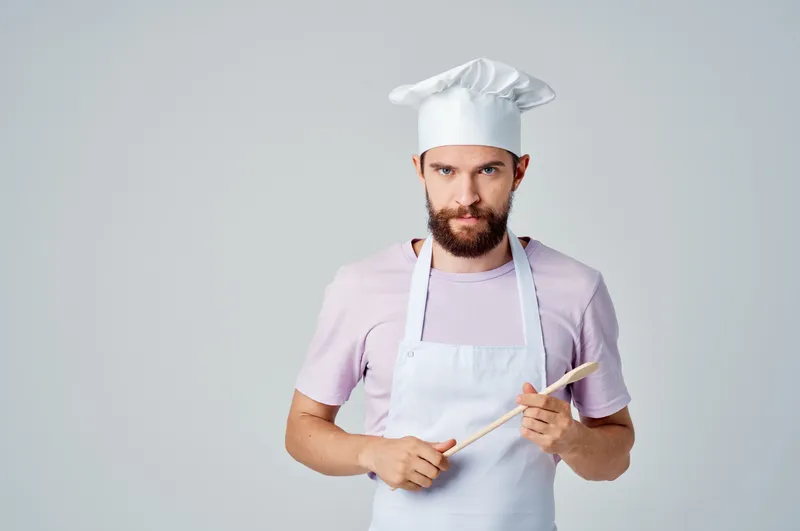 Профессиональный повар с деревянной ложкой в руке работает на кухне