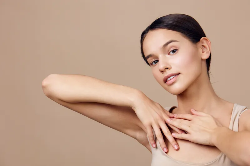 Portrait of a young woman with a natural expression, wearing a light tank top against a soft neutral background, emphasizing beauty and confidence