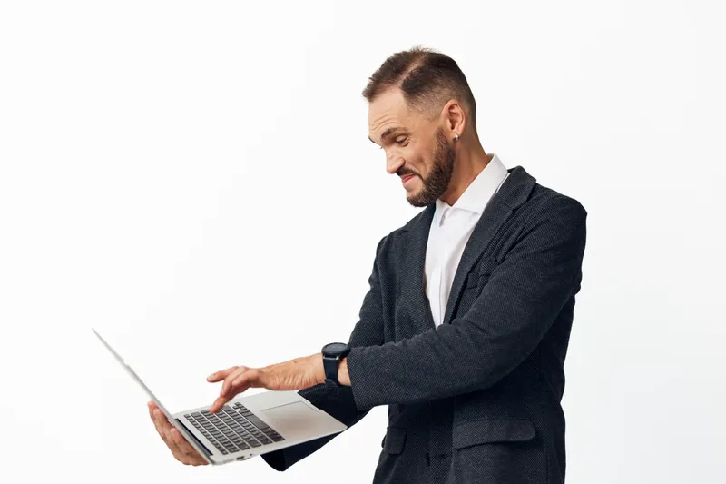 A professional man in business attire uses a laptop, showing confident emotions and focused energy on an isolated colored backdrop, suitable for corporate and tech themes.