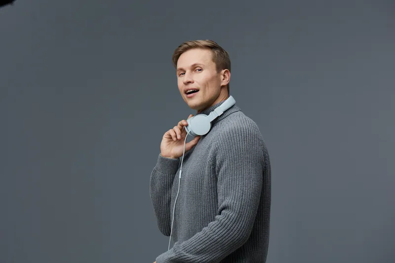 Smiling young man with headphones wearing casual sweater listening to music isolated on plain gray background studio portrait. People lifestyle concept
