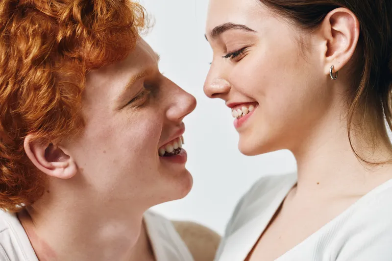 Couple, young man and woman smiling and facing each other for love, relationship and happiness indoors. People, emotion and affection with closeup of faces and positive connection between two adults.