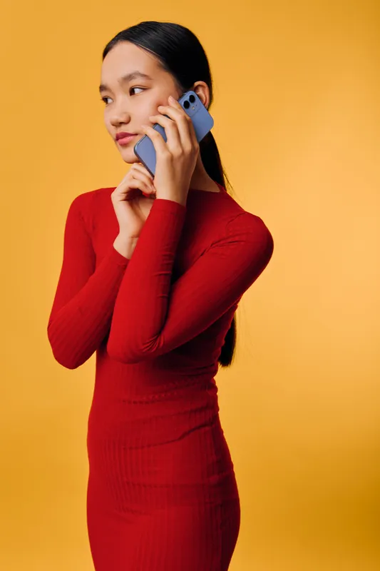 Woman in red dress talking on smartphone looking away on yellow background. Young female using mobile phone, communication technology, casual style and modern device.