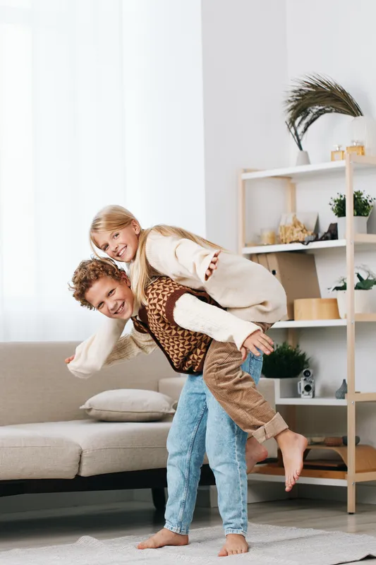 A playful couple shares a spontaneous piggyback moment in a bright living room, capturing cheerful energy, carefree laughter, and a warm, affectionate bond.