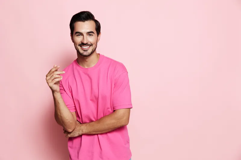 Smiling man wearing a bright pink t-shirt poses confidently against a solid pink background, showcasing a casual and cheerful lifestyle.