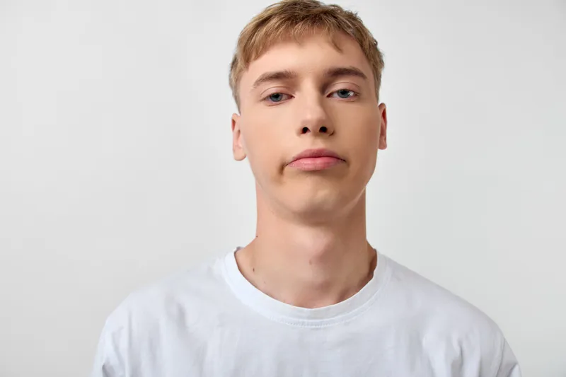 Young man headshots, white t shirt, studio, neutral expression, close up, plain background, minimal, casual, facial lighting, shot of model, warm hue.