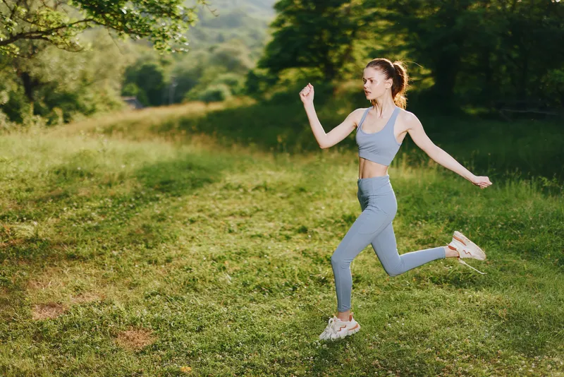 Joyful young woman jogging in stylish activewear on a sunlit green field, embodying a healthy lifestyle and fitness inspiration, perfect for sports concepts