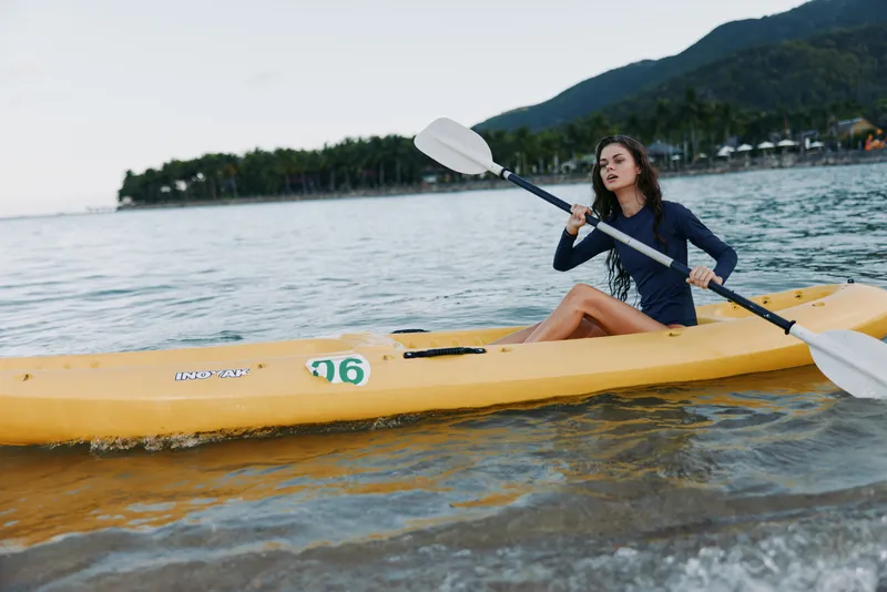 A female paddler sits in a bright yellow kayak, gliding across calm water with a double blade paddle, showcasing balance, focus, and outdoor adventure.