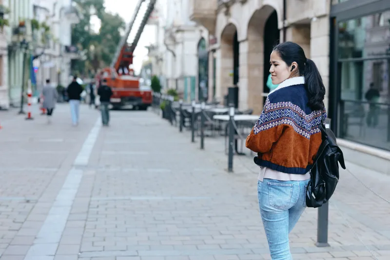 Woman with backpack walking along a city street, wearing a colorful knit sweater and jeans, urban street style, casual outing, contemporary fashion and everyday confidence