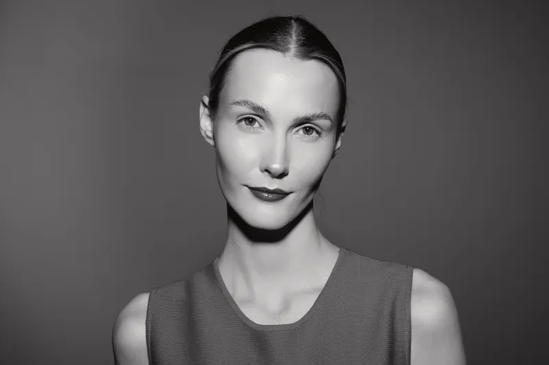 Portrait of a white woman with light skin and slicked back hair wearing a sleeveless top. Studio black and white photo with soft lighting and neutral background, beauty and fashion concept.