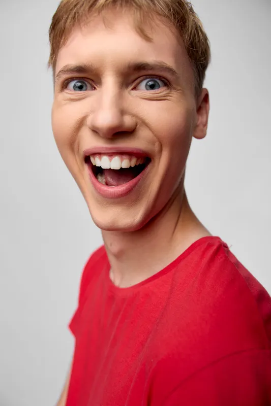 Excited, surprised, happy expression on a young man wearing a red shirt, closeup shot capturing energy, spontaneity and vibrant mood in a candid studio setting
