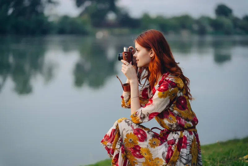 Женщина в разноцветном платье с фотоаппаратом в руках на открытом воздухе