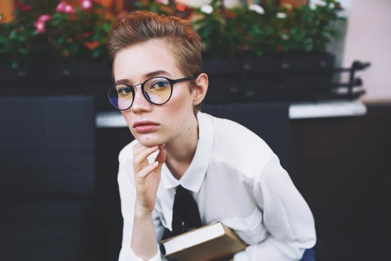 Коротко стриженная женщина стоит на улице с книгой в руках