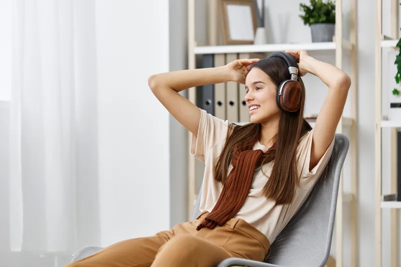 Молодая женщина в наушниках сидит в кресле и слушает музыку на MP3-плеере