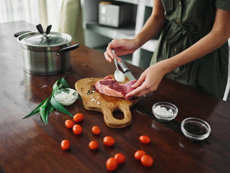 Женщина на кухне готовит ужин из мяса, овощей и специй на деревянном столе на фоне стильной кухни