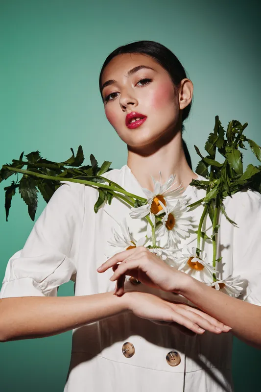 Fashion portrait of a young woman with bold makeup holding fresh daisies across her chest. Soft lighting enhances the artistic beauty and creative concept of floral elegance.