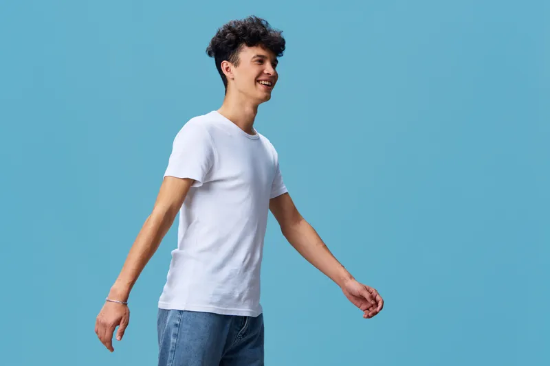 smiling man walking wearing white t-shirt and denim jeans against blue background, casual style with cheerful expression and relaxed posture in studio setting