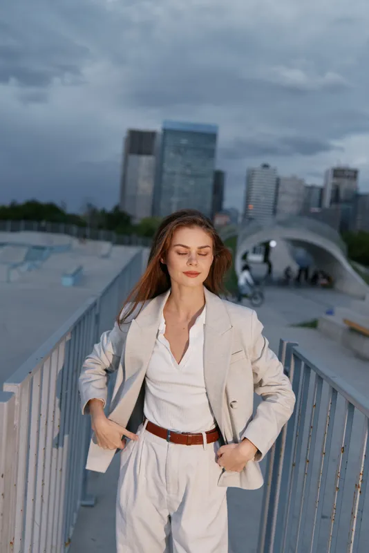 confident woman in light suit standing outdoors with cityscape background during cloudy weather urban business style