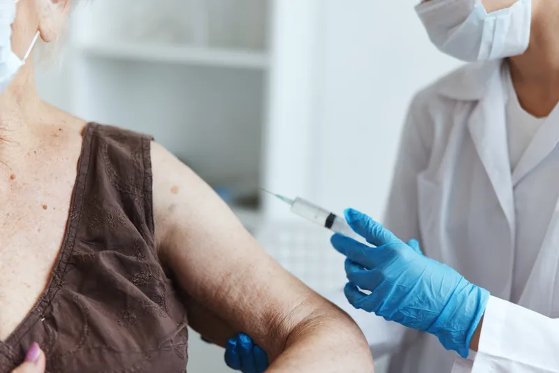 Врач со шприцем делает пациенту инъекцию вакцины, крупным планом виден паспорт вакцинации