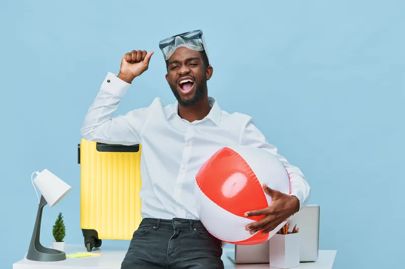 Joyful young man in casual white shirt holding a large inflatable heart at home, celebrating happiness with summer accessories on bright background. Cheerful emotions, lifestyle concept, fun, vacation