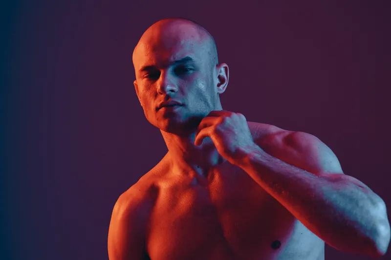Portrait of a confident man in dramatic lighting, showcasing a bold expression and highlighting his physique in a creative color palette.