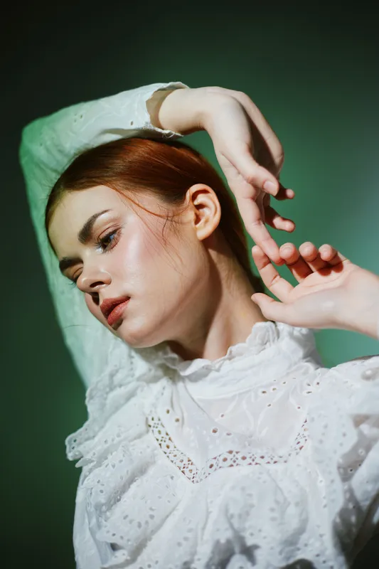 Artistic portrait of a young Caucasian woman with red hair in a white vintage dress, showcasing graceful poses against a soft green background