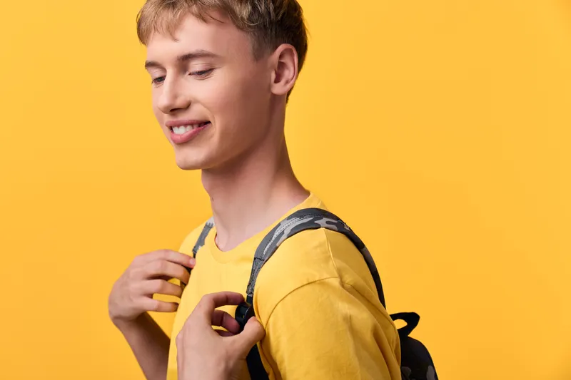 Student backpack youth casual smile yellow fashion lifestyle cheerful scene of a young learner with a backpack against a bright yellow backdrop, suitable for education, youth culture, street style