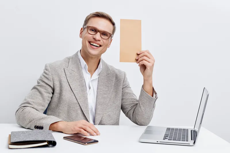smiling man working with laptop hold blank paper sheet wearing gray blazer glasses sit at table white background digital nomad concept