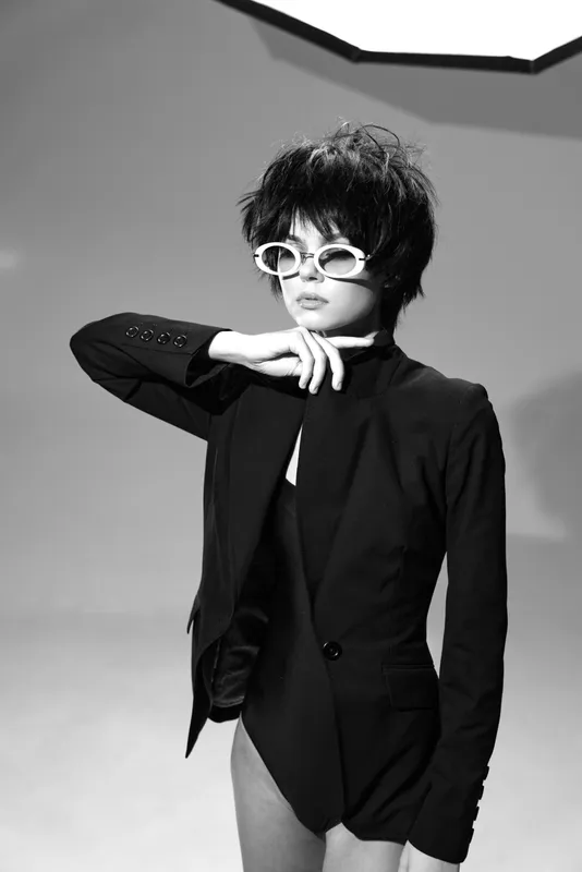 Stylish woman posing in black jacket and sunglasses in black and white studio setting