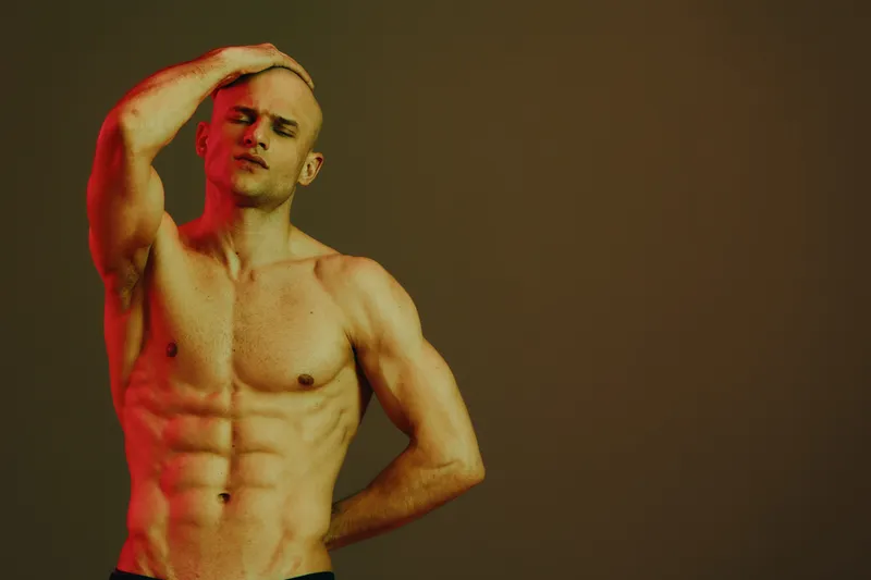 Confident man showcasing a muscular physique with dramatic lighting in a black and white composition, exuding strength and determination.