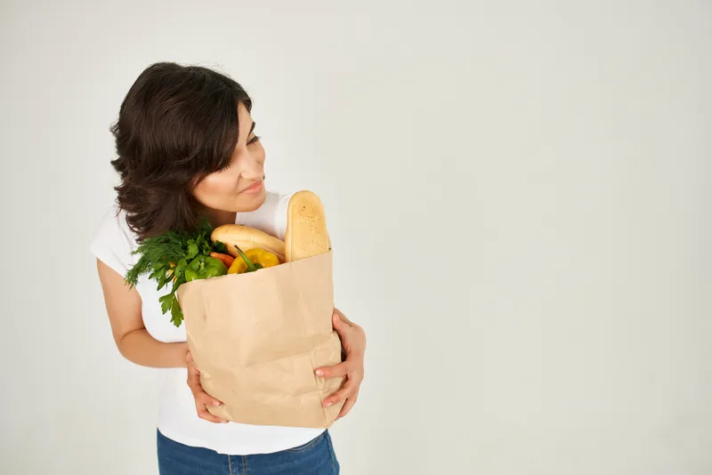 Милая брюнетка в белой футболке держит в руках пакет с продуктами из супермаркета